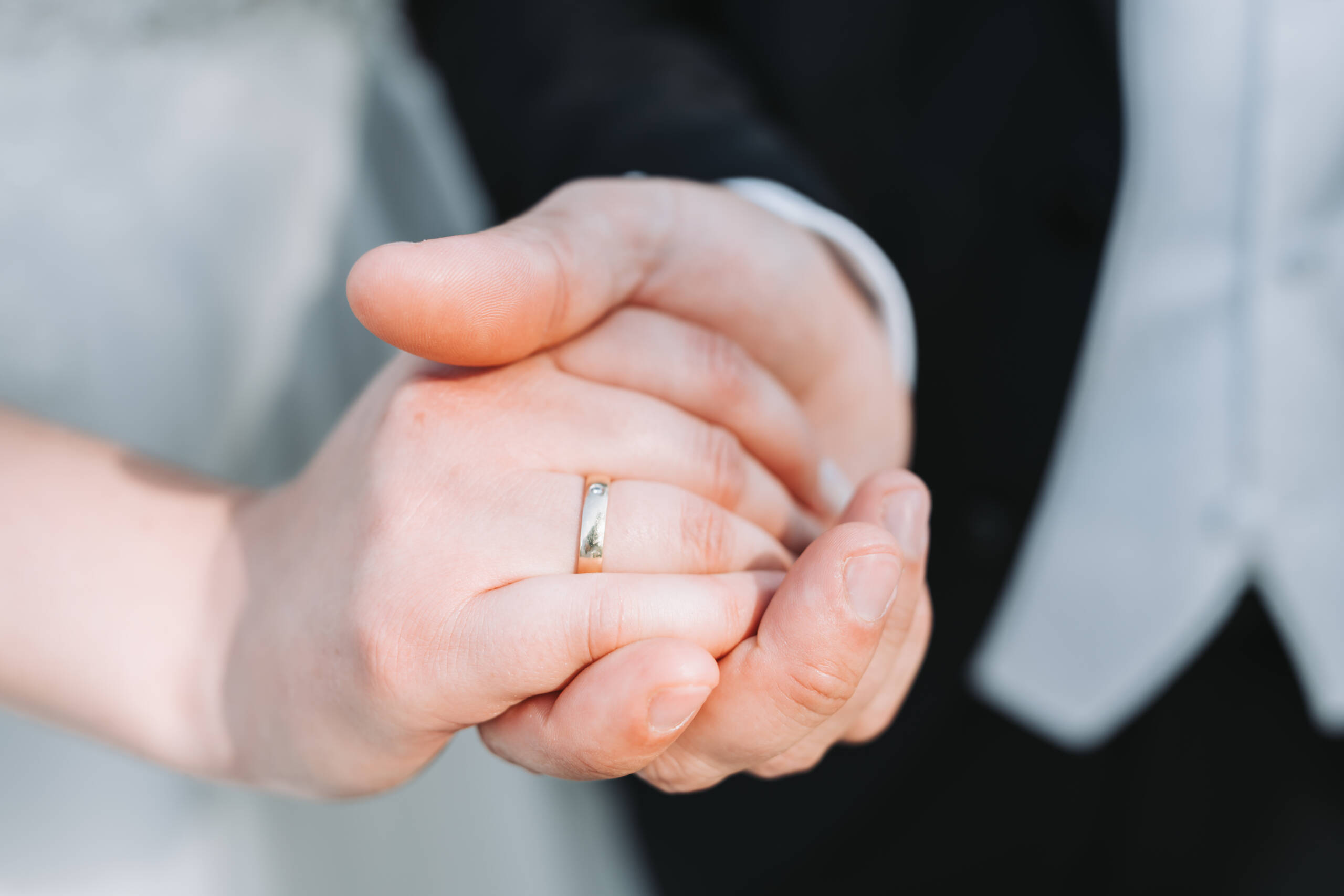 Ein frisch verheiratetes Brautpaar hält Hände und zeigt dabei den Ring am Ringfinger der Braut.
