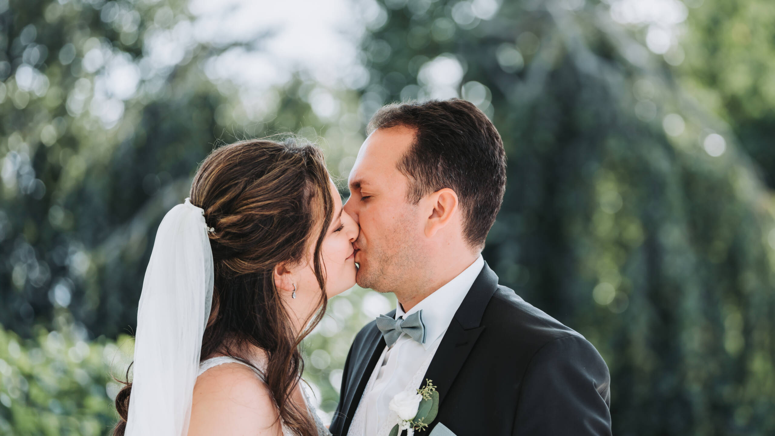 Ein frisch verheiratetes und verliebtes Hochzeitspaar steht in mitten der Natur und küsst sich mit vollen Emotionen. Das Foto wurde von einem Hochzeitsfotografen aus Neuss aufgenommen.