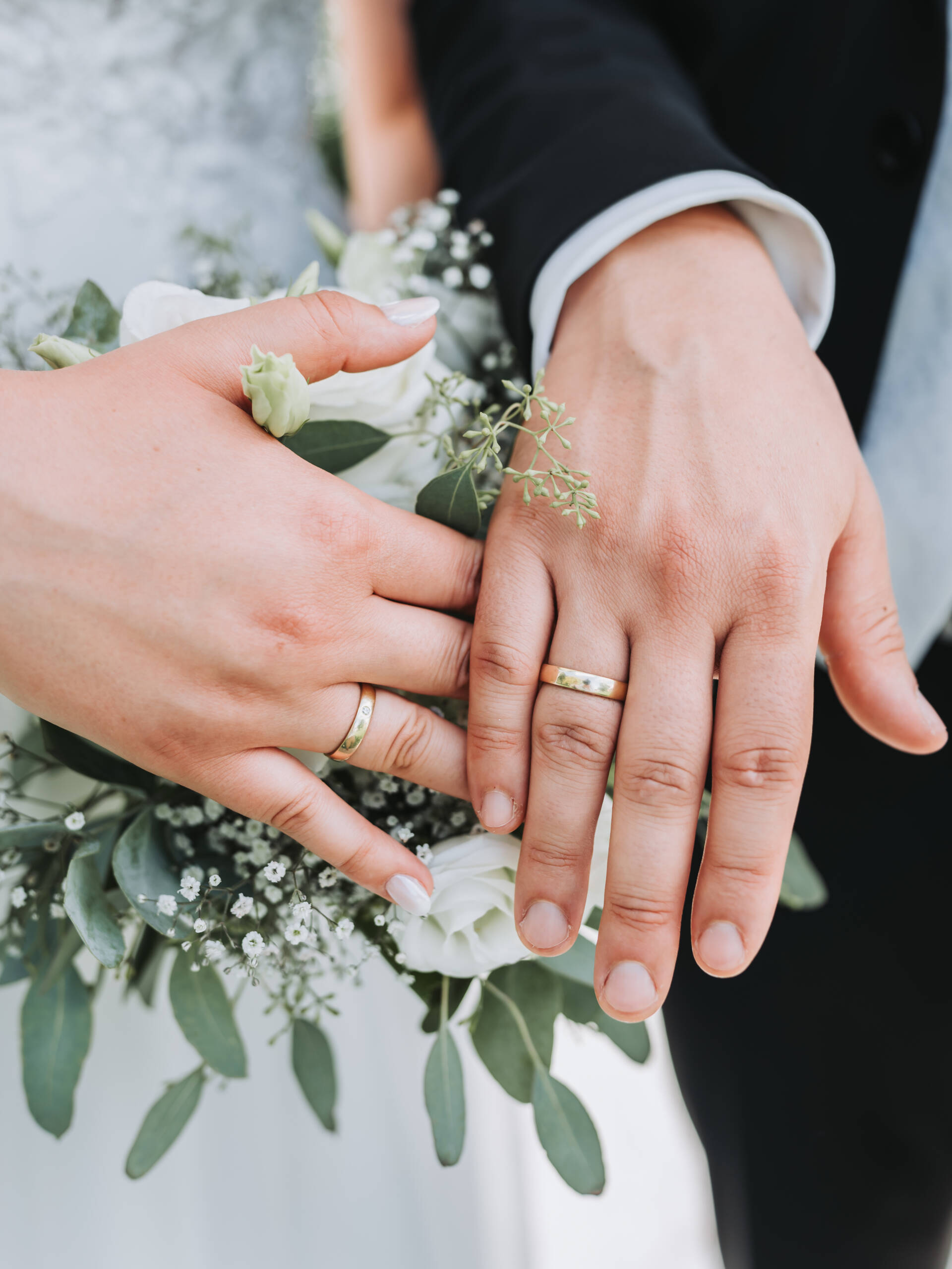 Ein frisch verheiratetes Brautpaar zeigt mit Stolz die Eheringe und hält diese über den Brautstrauß.