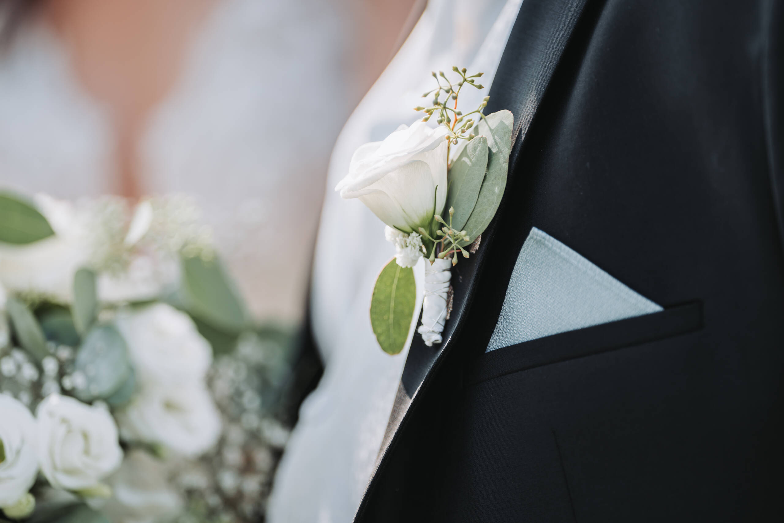 Eine Detailaufnahme des grün weißen Blumenschmuckes am Sakko des Bräutigams.