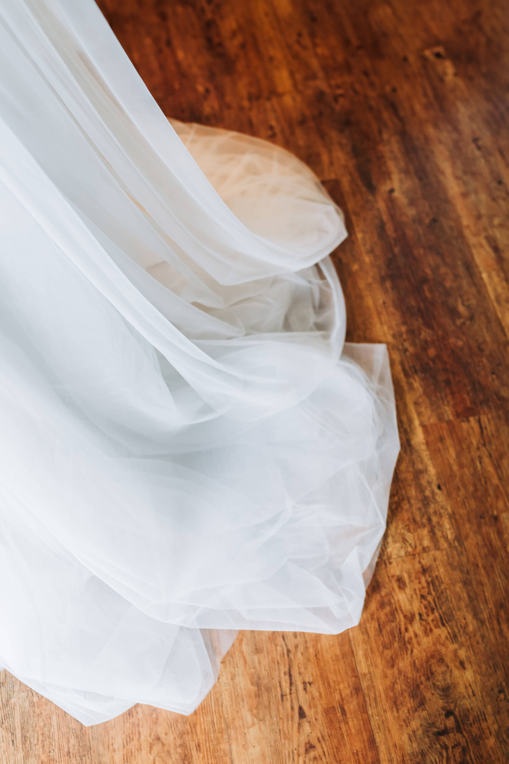 Die Schleppe eines strahlend weißen Brautkleides welches auf einem wunderschönen alten Holzfußboden liegt.